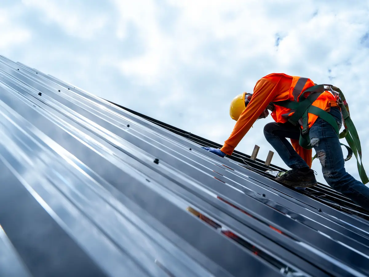 Roofer in a safety harness working on a metal roof