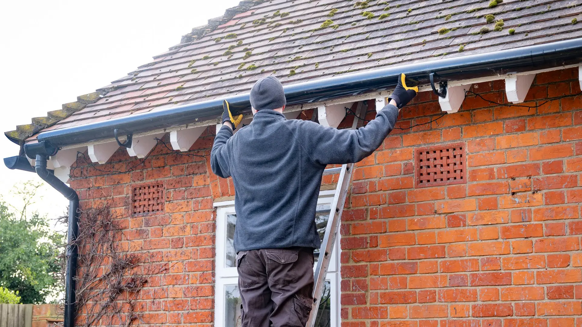Gutter being cleared and repaired on a brick cottage