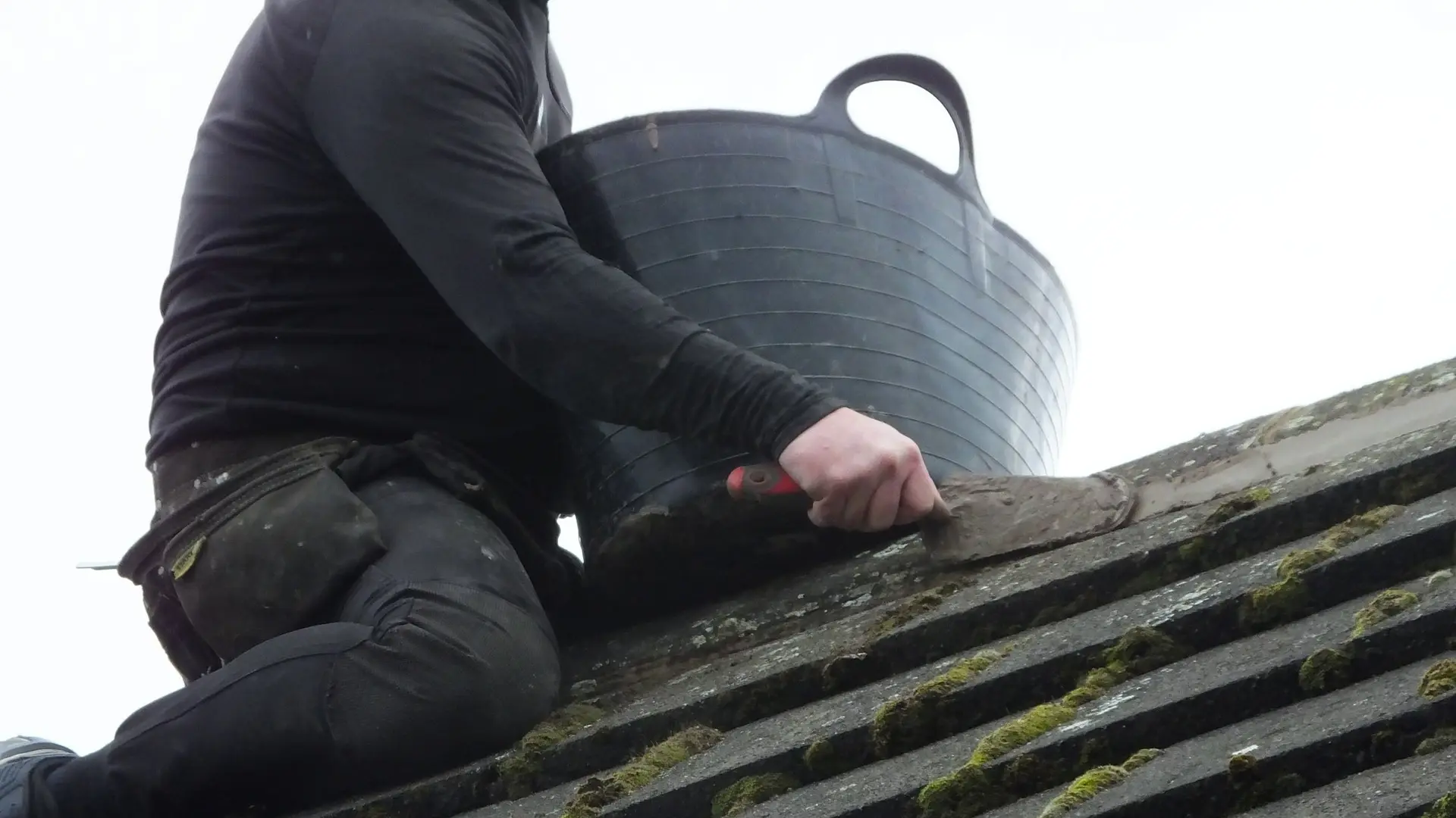 Roofer removing moss from a roof by hand