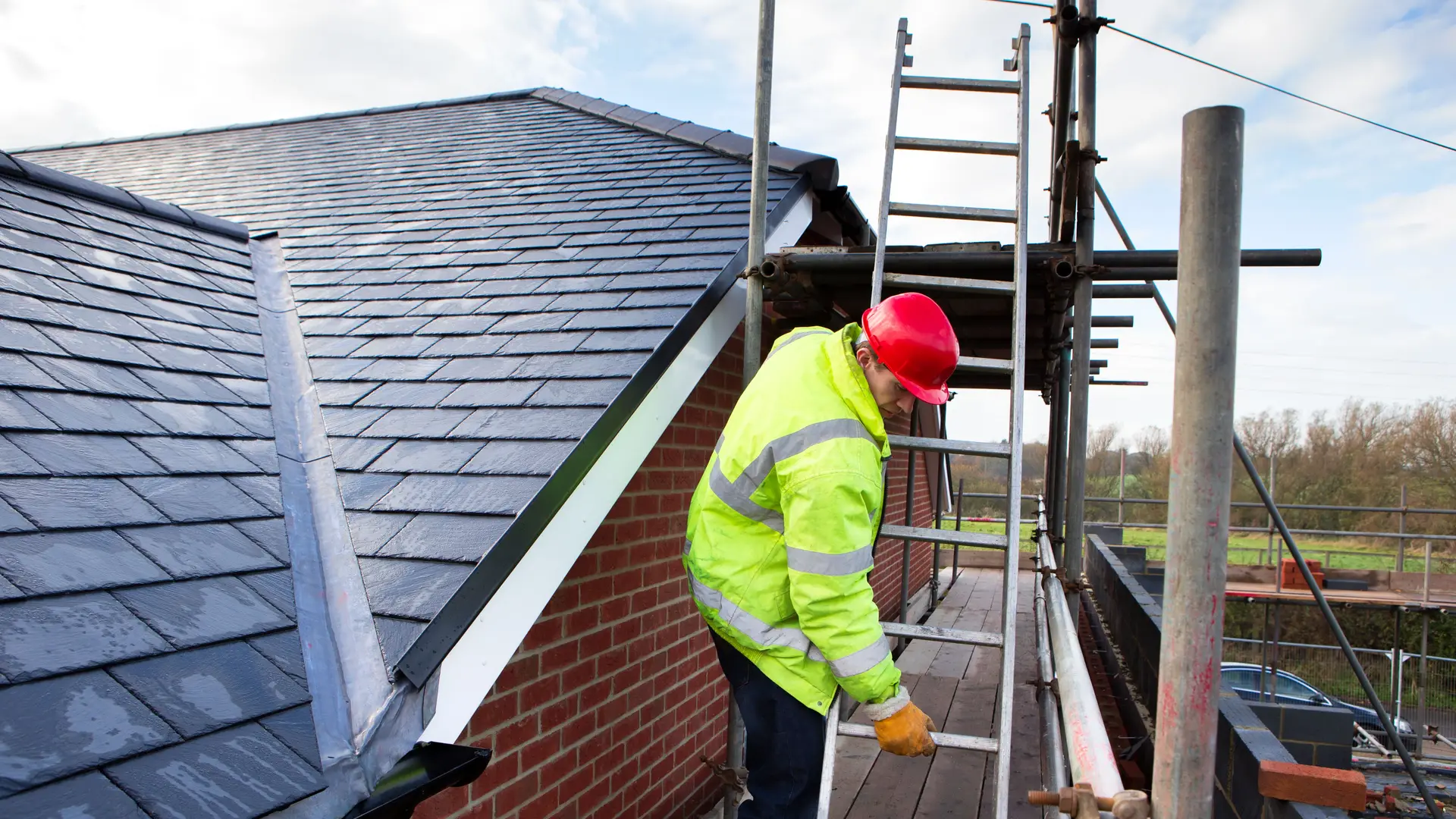 Roofer on scaffolding beside a newly laid slate roof